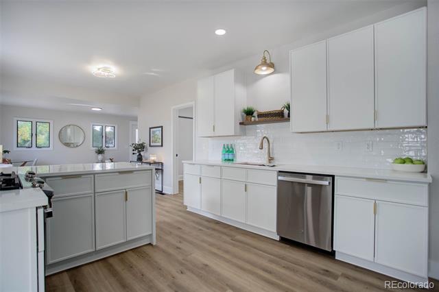 Bright white kitchen with a large island, stainless steel dishwasher, and light wood flooring.