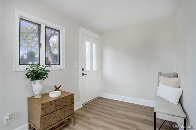 Bright entry room with a white door, wood-look flooring, geometric dresser, and cushioned chair.