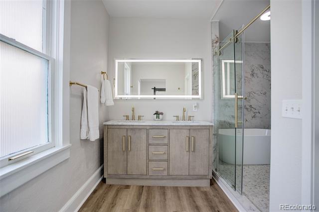 Bathroom with a gray double vanity, wood-look flooring, and a glass-enclosed marble-look shower.