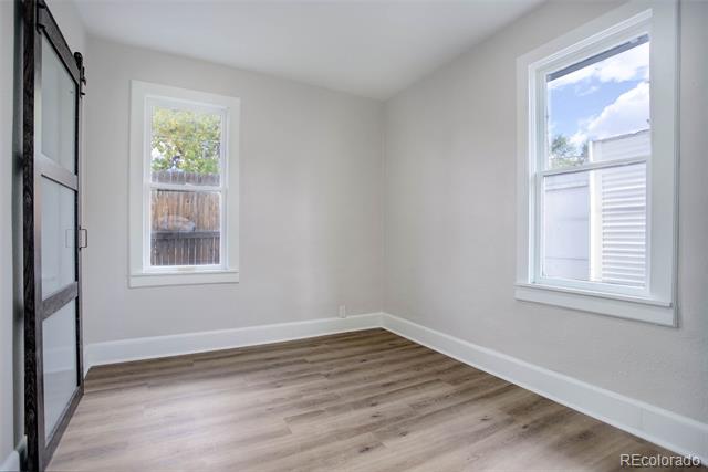 Vacant room with wood-look flooring, two windows, and a dark-framed sliding closet door.