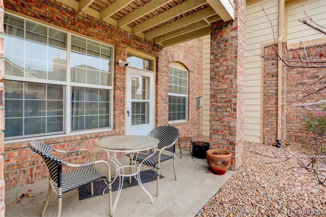Covered brick patio with a metal café table and chairs beside large windows and a glass-paneled door.