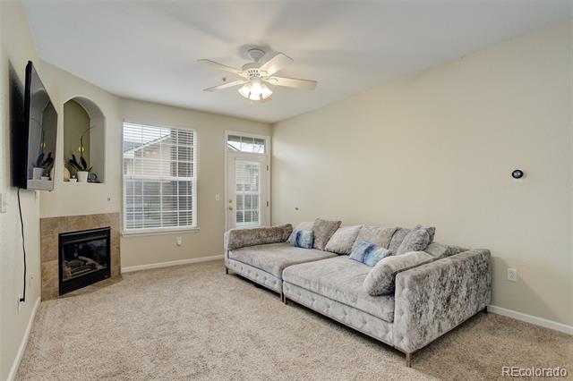 Living room with a gray sectional sofa, beige carpet, ceiling fan, and fireplace.