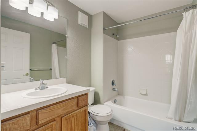 Bathroom with a white tub and shower curtain beside a wood vanity, sink, and toilet.