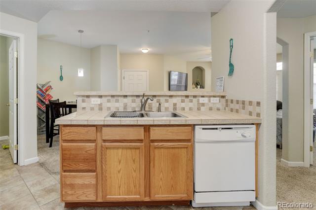 Kitchen with a wood-front peninsula, tiled counters, double-basin sink, and white dishwasher.