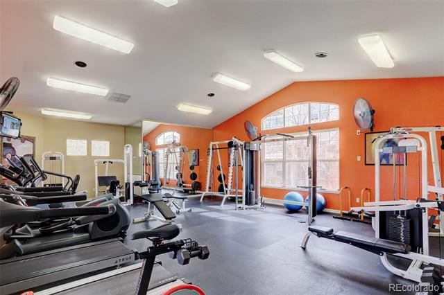 Fitness center with treadmills and weight machines beside large windows and orange walls.