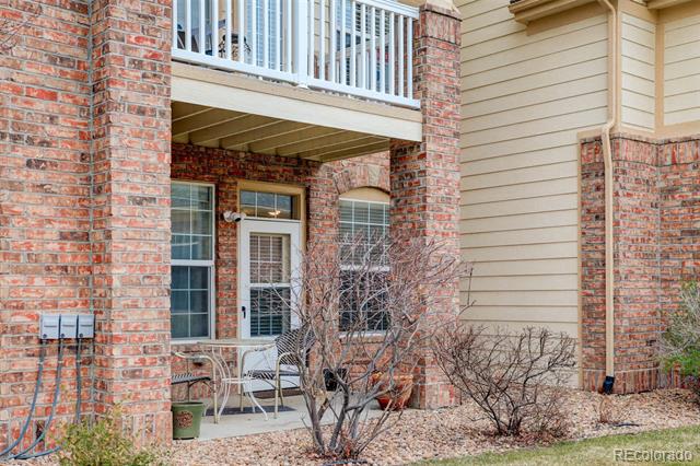 Residence exterior with a covered patio, brick columns, beige siding, and a balcony above.