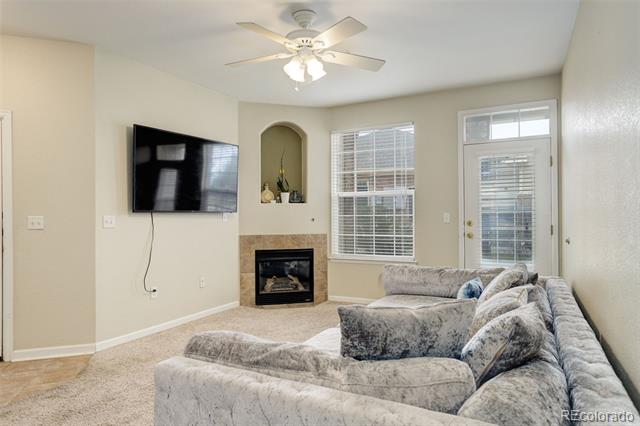 Living room with a gray sectional, tiled fireplace, wall-mounted TV, and glass-paneled door.