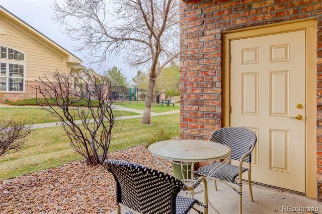 Patio with round table and woven chairs beside a brick wall, overlooking a landscaped courtyard.