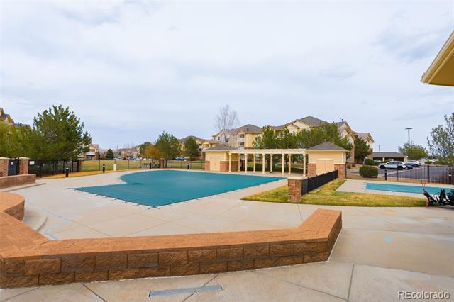 Outdoor community pool with a wide paved deck, brick seating walls, and a pergola.