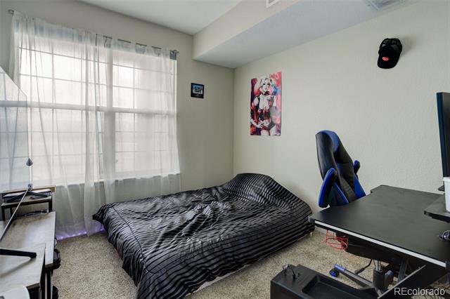 Bedroom with striped bedding, a large curtained window, and a gaming chair beside a desk.