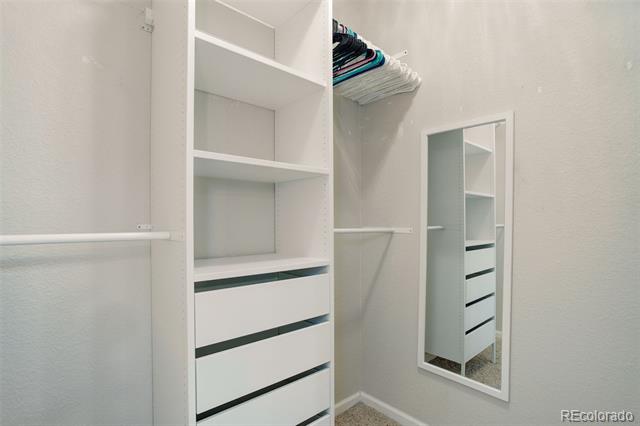 Walk-in closet with built-in shelves and drawers, hanging clothes, and a full-length mirror.