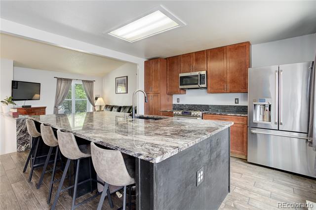 Kitchen with a large stone island, breakfast bar seating, wood cabinets, and stainless steel appliances.