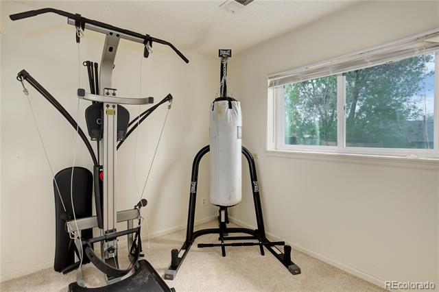 Home exercise room with a multi-station weight machine and hanging punching bag beside a wide window.