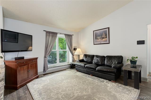 Living room with a black leather sofa, patterned rug, and curtained window overlooking greenery.