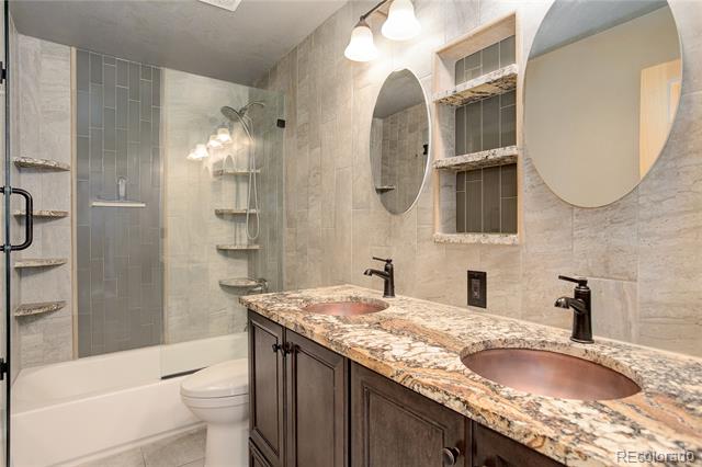 Bathroom with a double vanity, oval mirrors, and a tiled tub and shower.