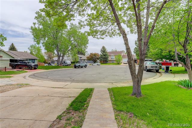 Suburban cul-de-sac with parked cars, leafy trees, and a brick walkway leading toward the street.
