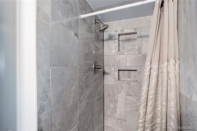 Tiled bathroom shower with two recessed niches and a light patterned curtain.