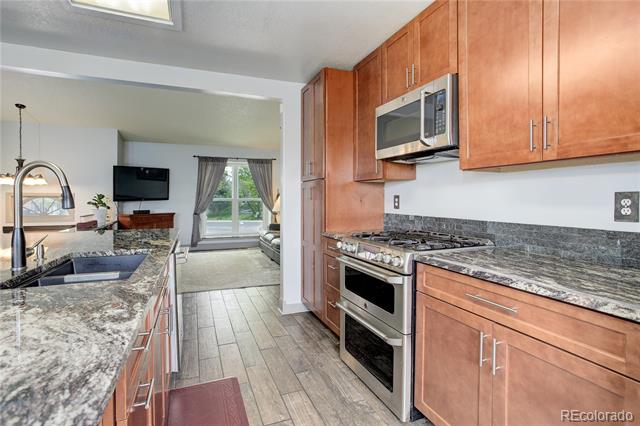 Kitchen with reddish wood cabinetry, a stainless steel range, and an island opening to the living area.