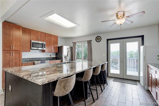 Kitchen with a granite island and bar stools, wood cabinets, and glass doors to a deck.