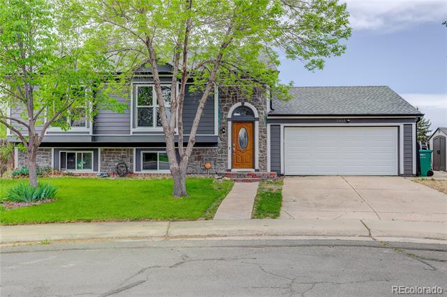 Gray two-story house with stone accents, wooden front door, double garage, and leafy front yard.