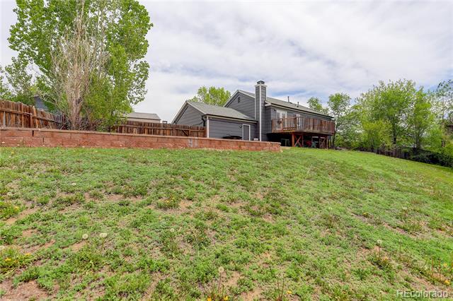 Gray two-story house with a raised deck beyond a brick retaining wall and sloping lawn.