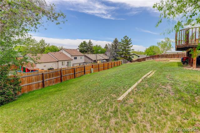 Grassy backyard with a wooden fence, neighboring homes, and a raised deck.