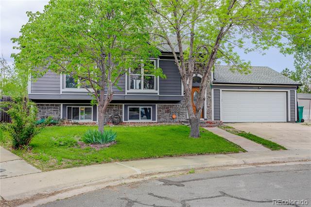Split-level home with gray siding, stone accents, and a two-car garage behind mature trees.
