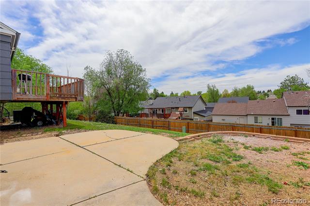 Backyard patio and raised wooden deck beside a fenced yard and neighboring homes.