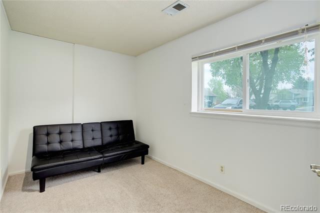 Carpeted room with a black tufted sofa beneath a wide window.
