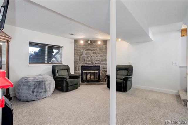 Living room with a stone fireplace, dark armchairs, and a gray pouf.