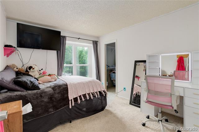 Bedroom with a dark upholstered bed, large window, wall-mounted television, and white vanity desk.