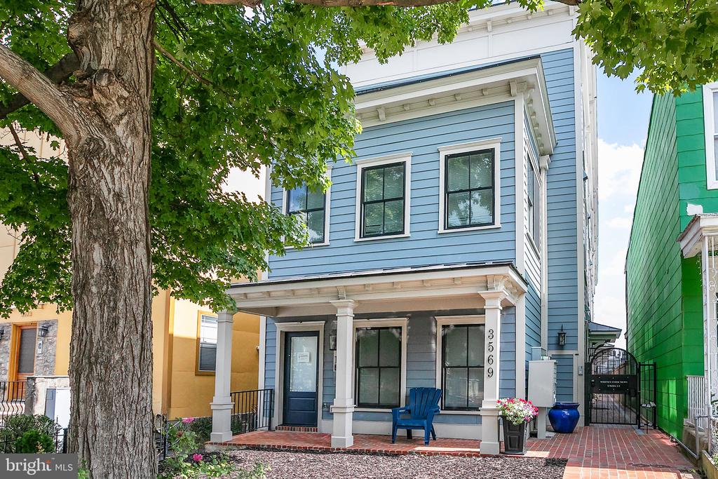 Blue two-story home with white trim, covered porch, brick walkway, and large tree in front.