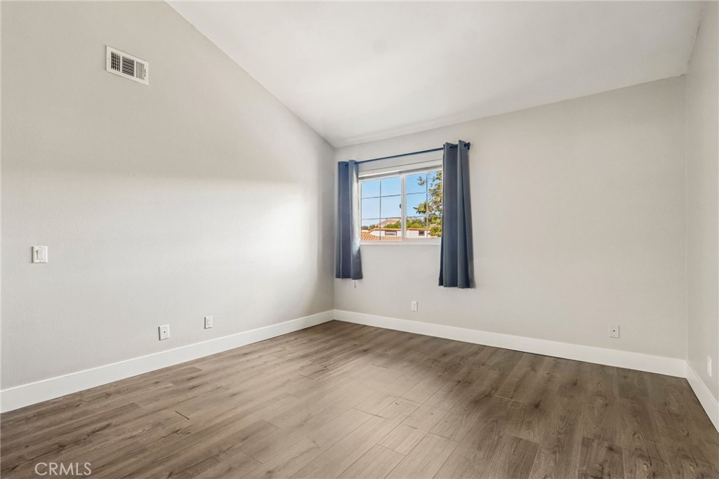 Empty room with wood-look flooring, high ceiling, and a curtained window.