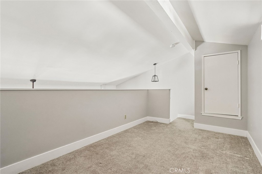Empty carpeted loft with a low half wall and a hanging light.