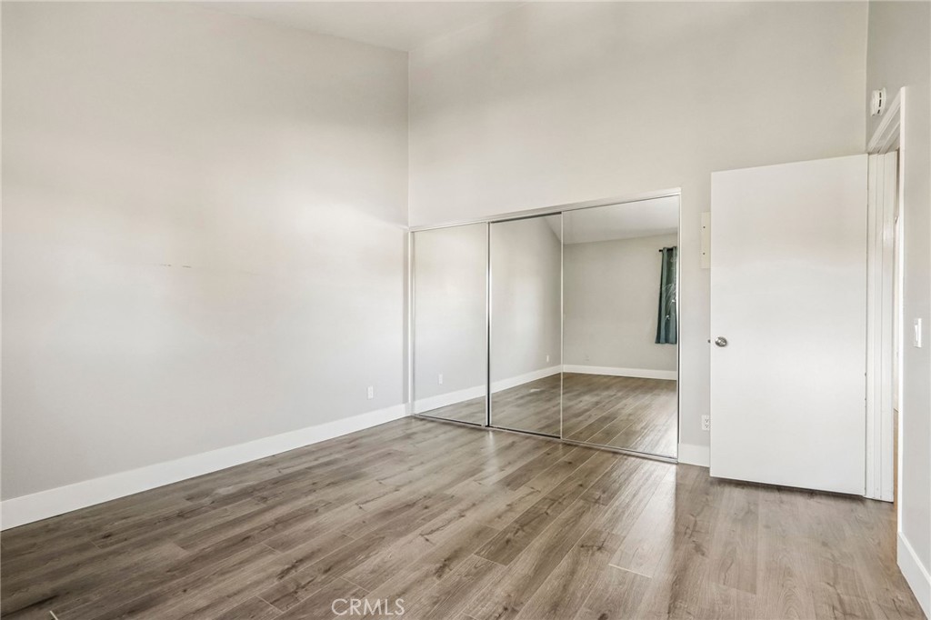 Empty bedroom with wood-look flooring and mirrored sliding closet doors.