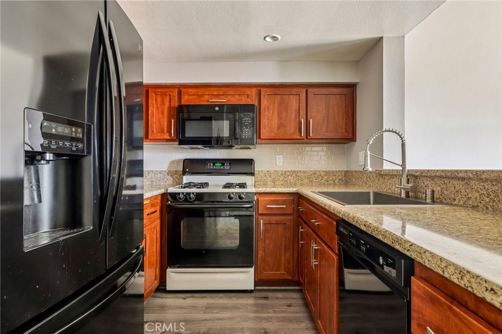 Kitchen with reddish wood cabinets, granite counters, stainless steel appliances, and a spring-coil faucet.