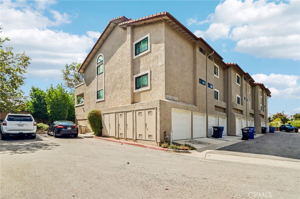 Multi-story stucco residential building with rows of garage doors and a paved parking area.