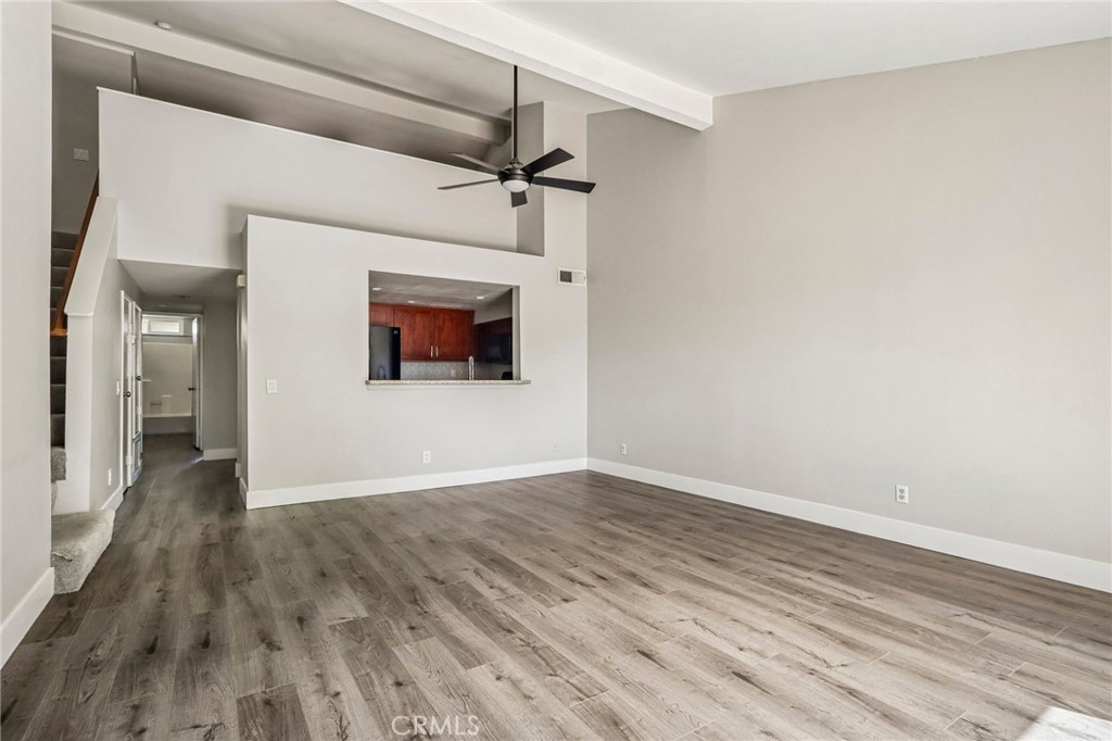 Empty living room with gray wood-look floors, high ceilings, a ceiling fan, and a kitchen pass-through.