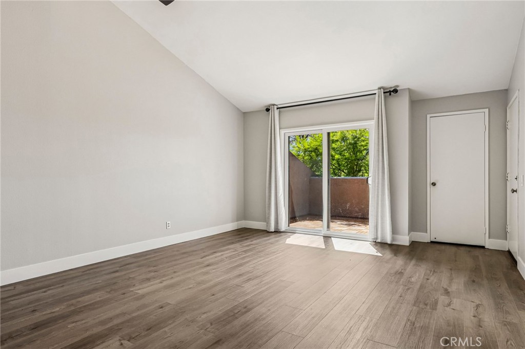 Empty room with wood flooring, a curtained sliding glass door, and a closet door.