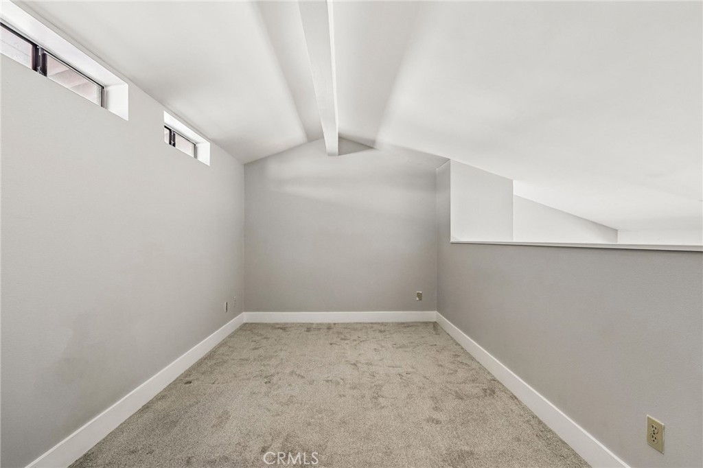 Empty carpeted loft with a sloped ceiling and small high-set windows.