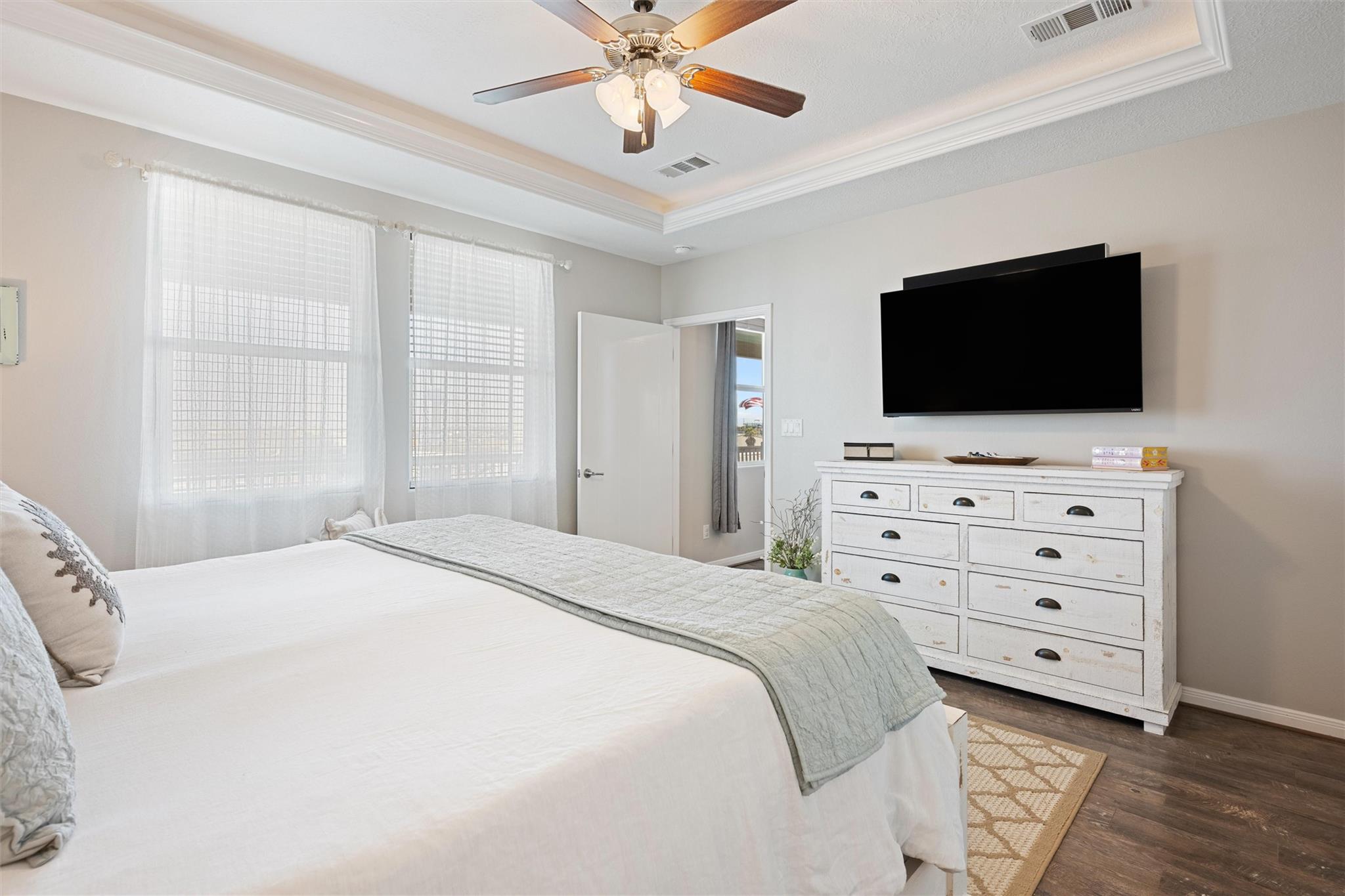 Bright bedroom with a large white bed, curtained windows, and a wall-mounted television.