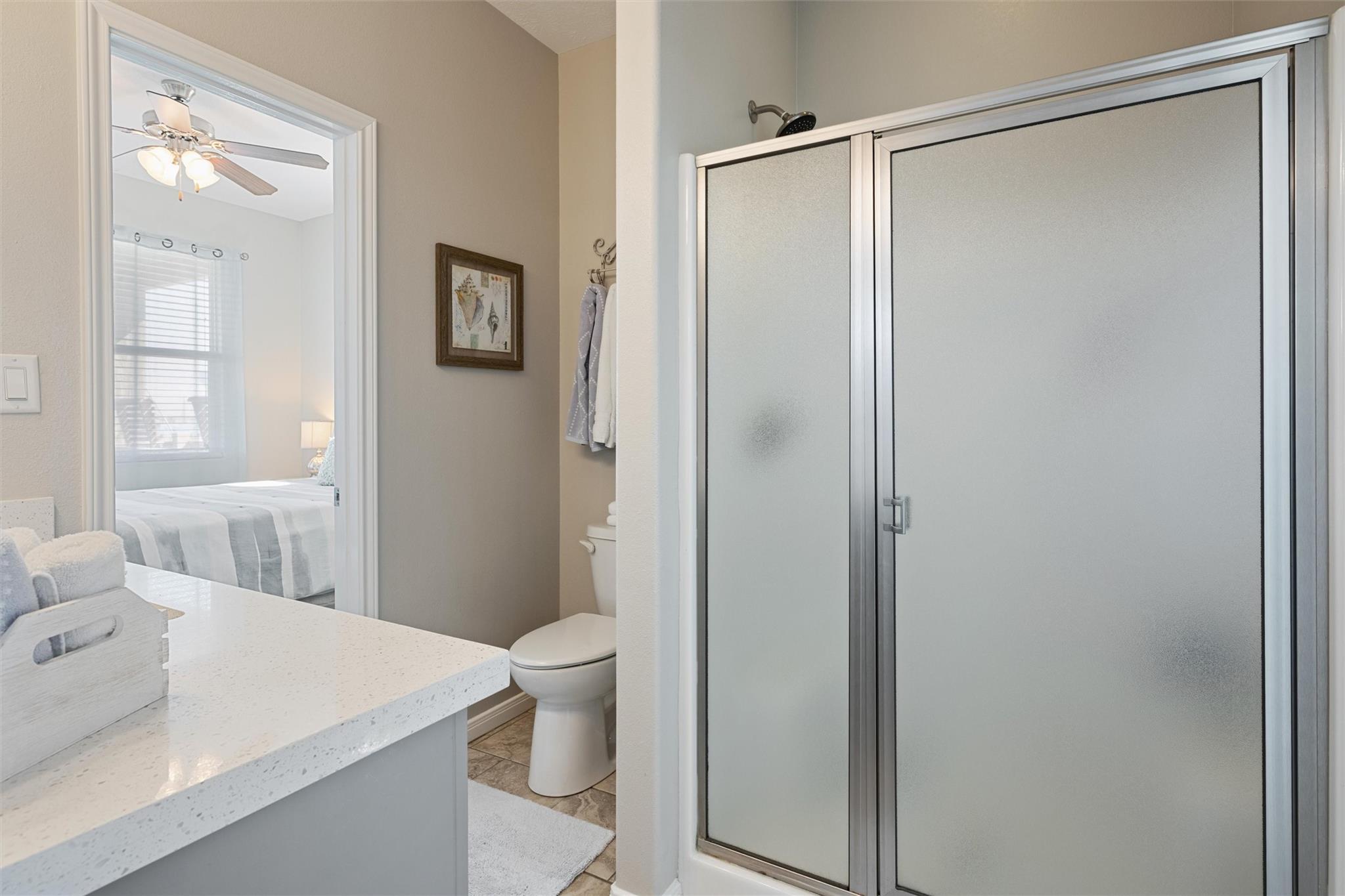 Bathroom with a frosted-glass shower enclosure, white vanity, and bedroom visible through the doorway.