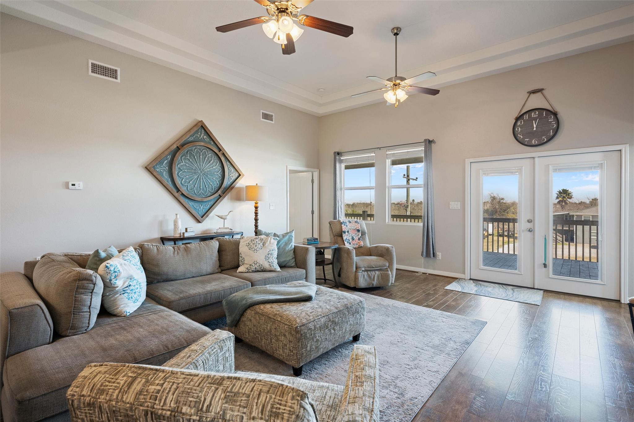 Furnished living room with a gray sectional, patterned cushions, and glass doors opening to a deck.