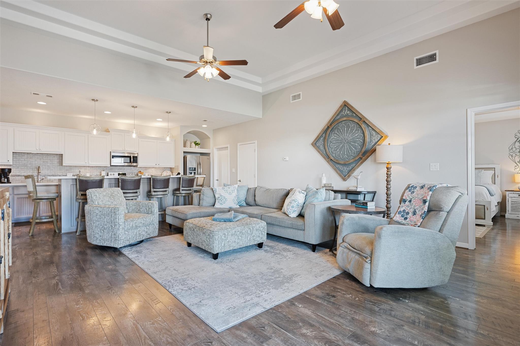 Open-plan living room with gray sectional seating and a white kitchen with breakfast bar.