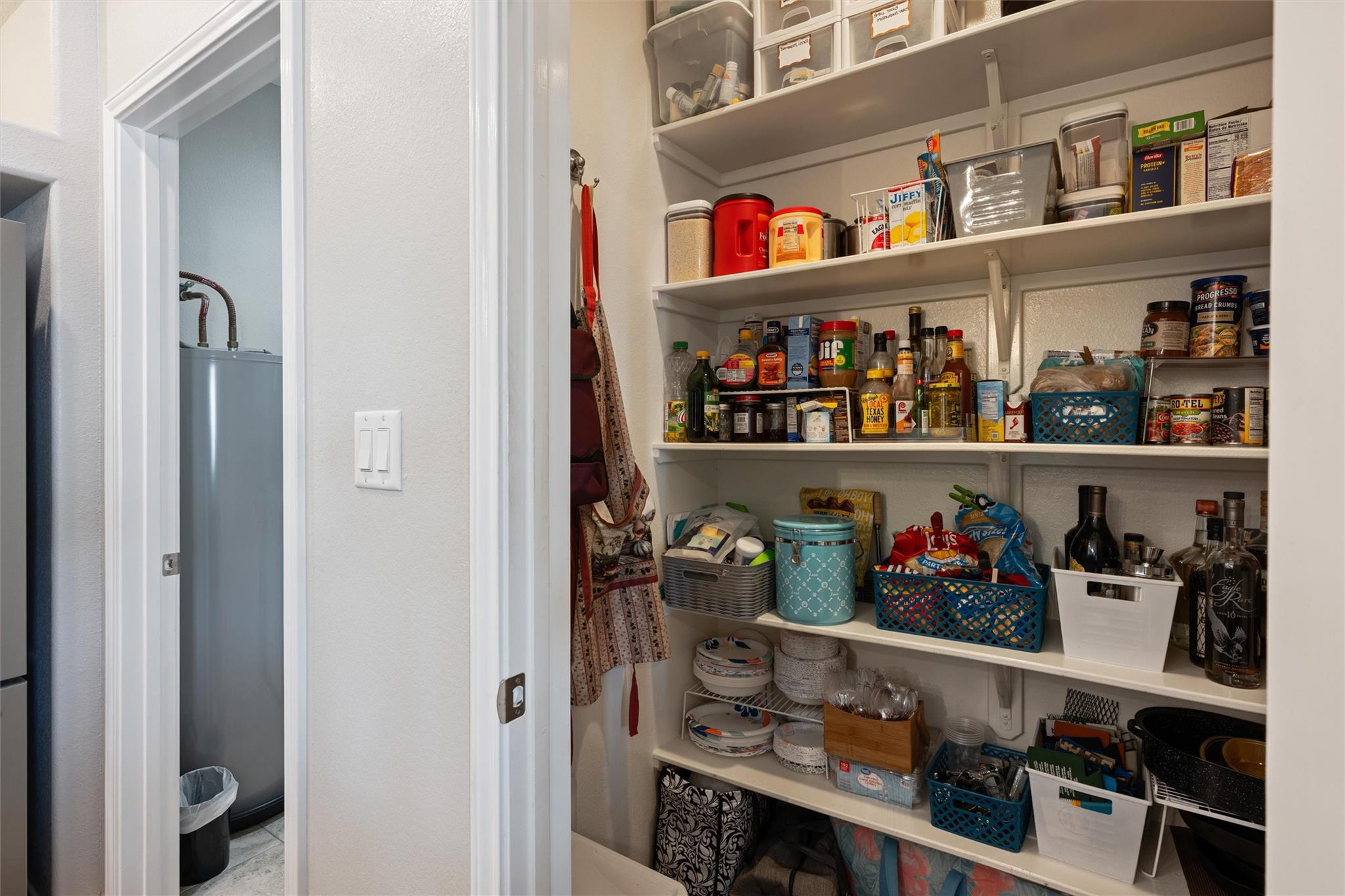 Walk-in pantry with stocked open shelves, storage baskets, and a utility-room doorway