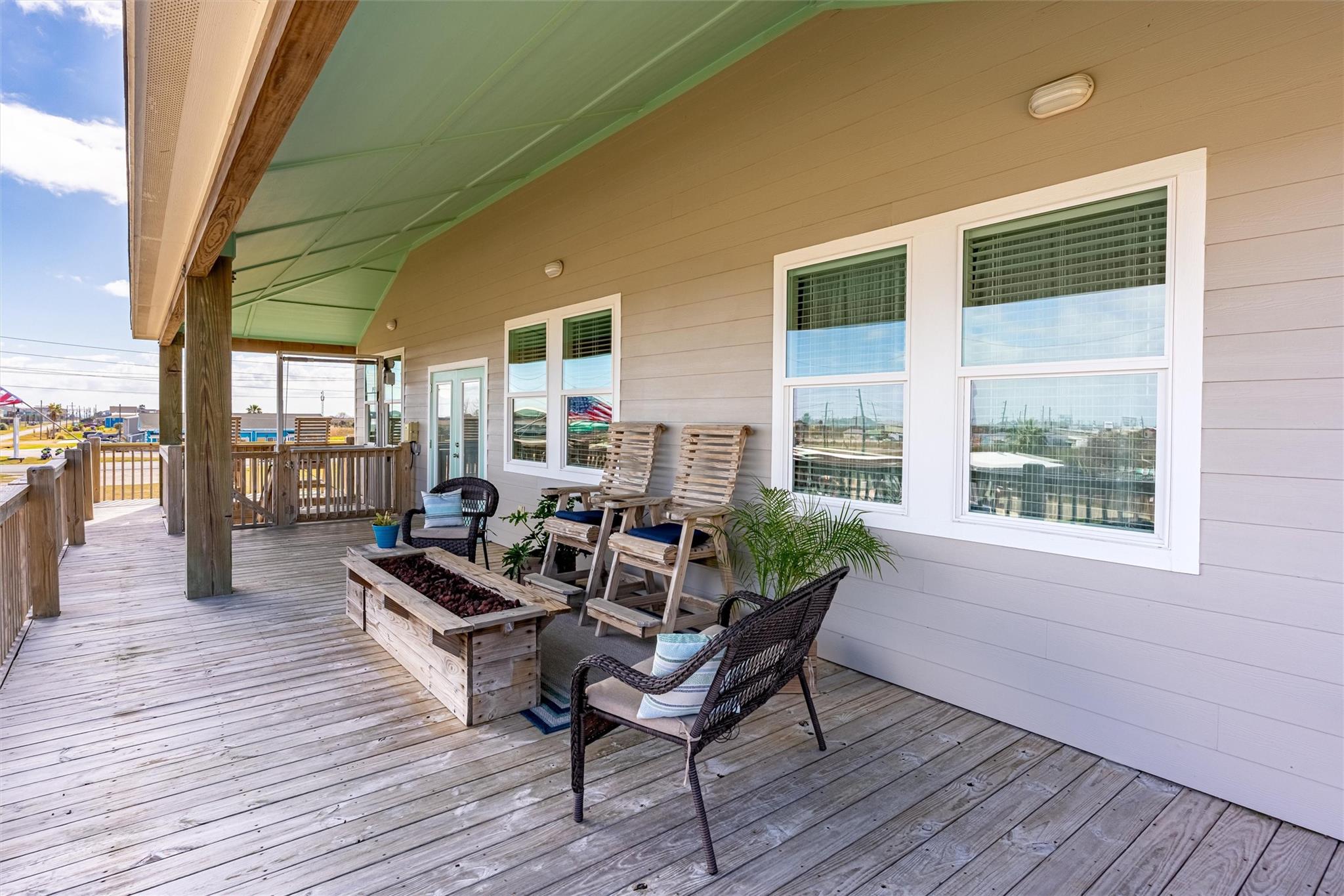 Covered wooden porch with lounge chairs, wicker seating, and large white-trimmed windows.