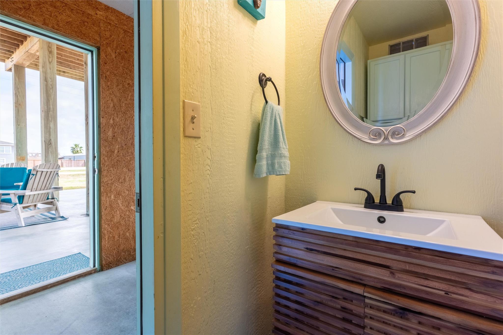 Bathroom vanity with a round mirror and open doorway to a covered patio.