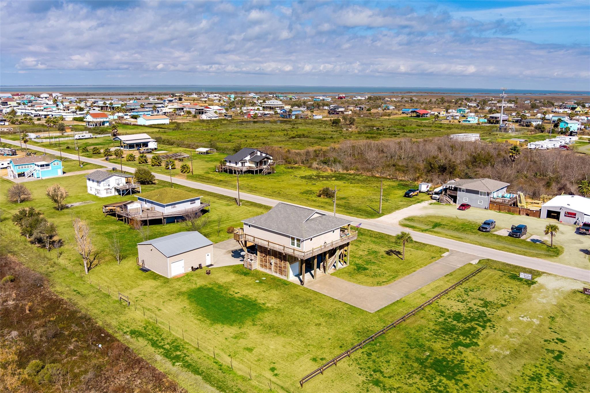 Elevated coastal home with a wraparound deck and detached garage on a large grassy lot near the water.