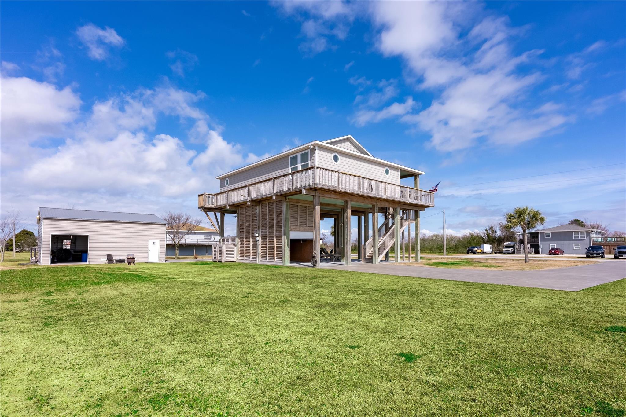 Raised coastal house with a wraparound deck and detached garage on a broad lawn.