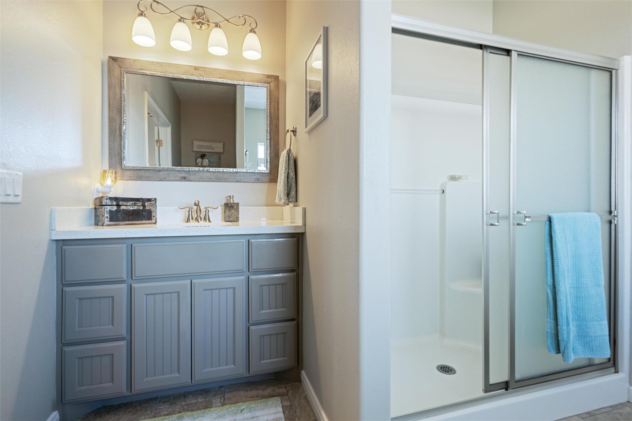 Bathroom with gray vanity and glass-enclosed shower; a blue towel hangs over the shower door.